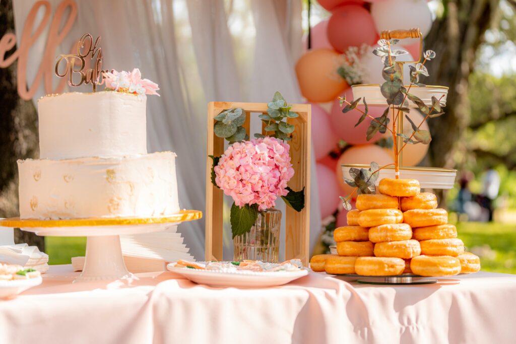 A beautifully decorated outdoor dessert table set for a baby shower featuring a cake and donuts.